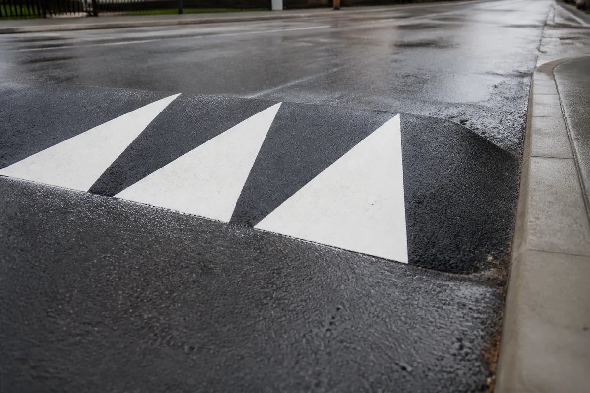 Ralentisseur trapézoïdal peint en blanc sur une rue résidentielle avec signalisation verticale