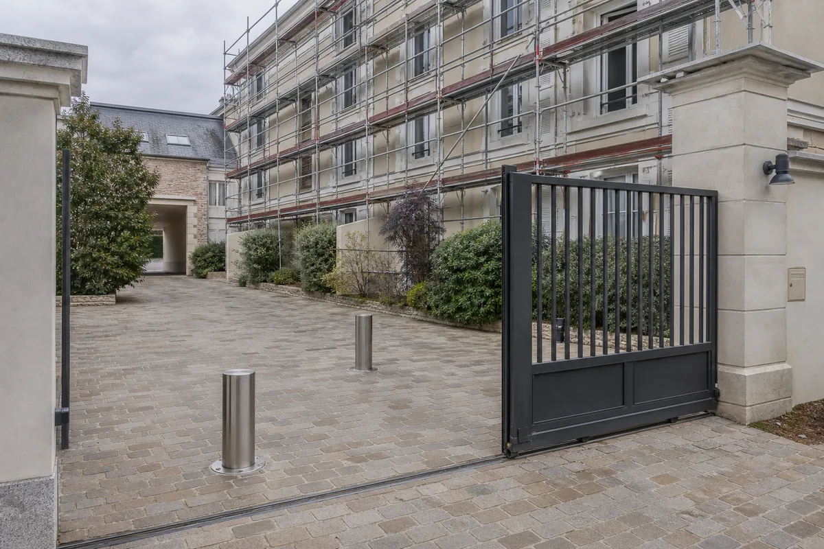 Cour intérieure de résidence avec portail et bornes escamotables, échafaudage en fond
